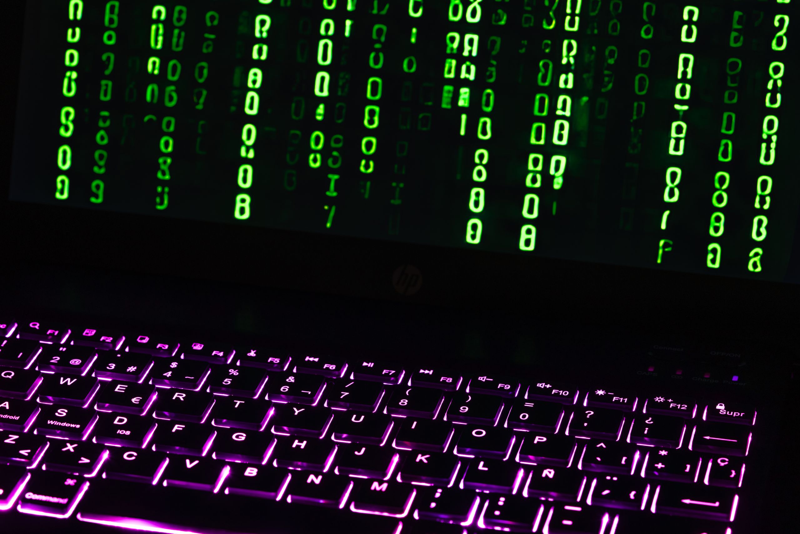 Illuminated laptop keyboard with Matrix-style green code cascading down screen.